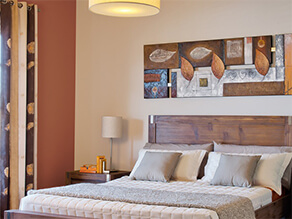 Neutral bedroom with brown artwork and dark wooden bedhead and brown wall and cream bedding pillows